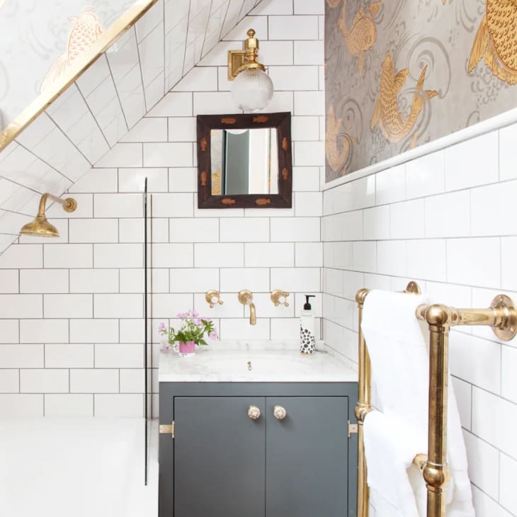 a white bathroom with white subway tiles, a small mirror, and gold accents