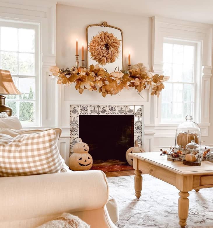Living room with fireplace decorated with faux fall leaves, pale orange candles, and other pumpkin and fall decor around