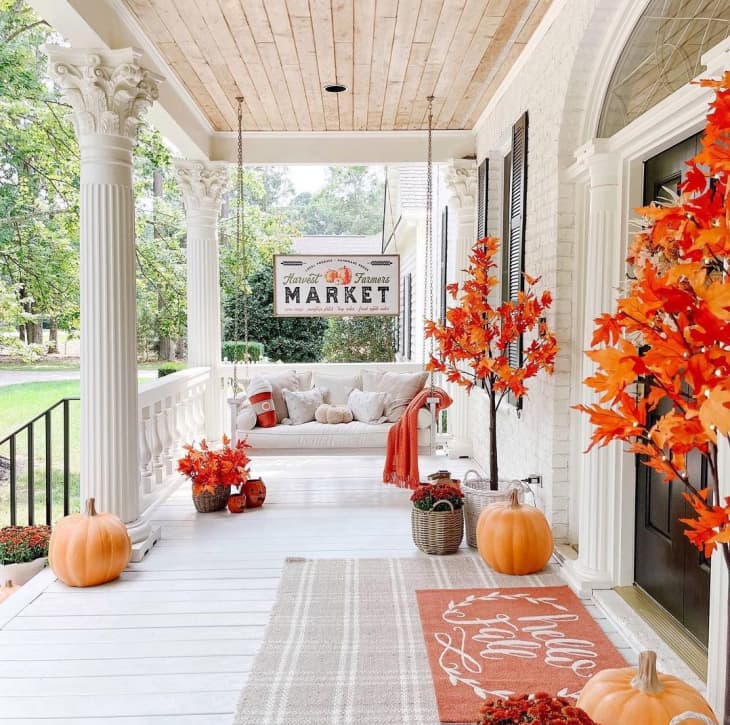 Front porch of home with fall doormat, faux small maple trees with orange leaves, and pumpkins