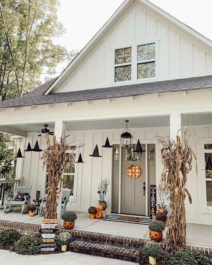 Front of house with dried cornstalk decor, hanging witch hats, and pumpkins