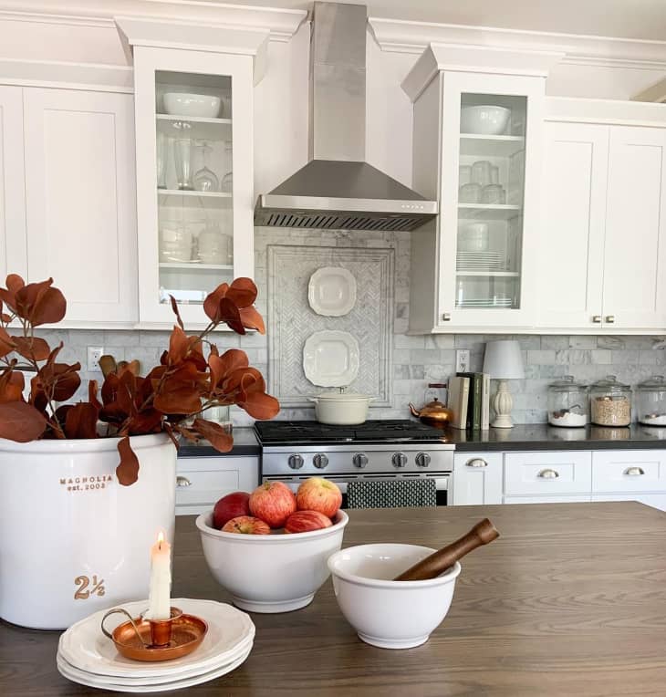 Kitchen with dried leaf branches in canister, bowl of apples, and candle with vintage copper candle holder