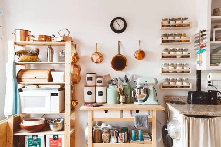 a vintage-looking kitchen with pots and pans hanging on the wall and shelves of kitchen utensils