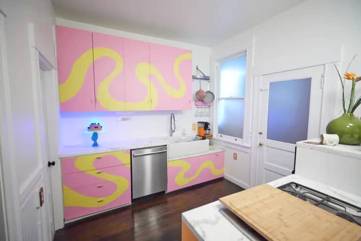 a white kitchen with painted pink and yellow abstract cabinets