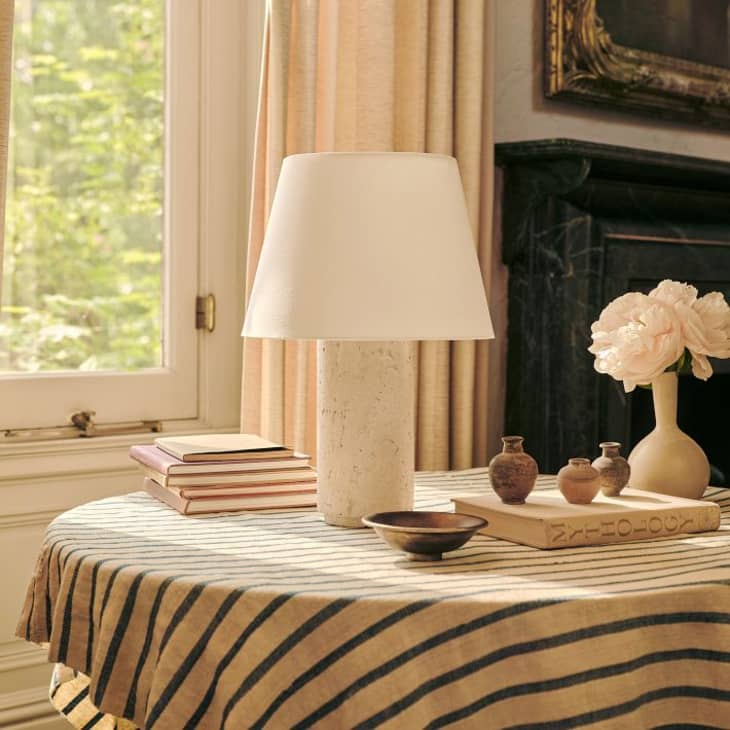 black and white striped table clothe, white lamp, white flowers, window, beige curtains, mantle, round table, books, small pottery dishes