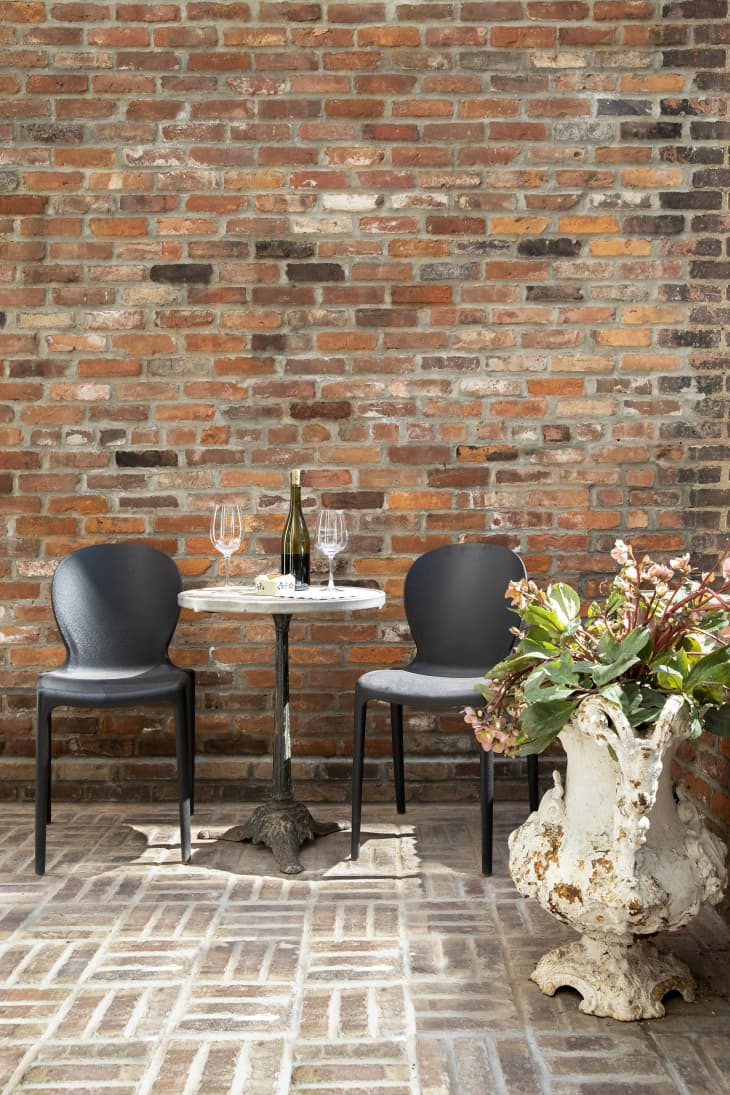 exposed brick, brick parquet floor, black patio chairs, small round marble table, large floor vase with flowers