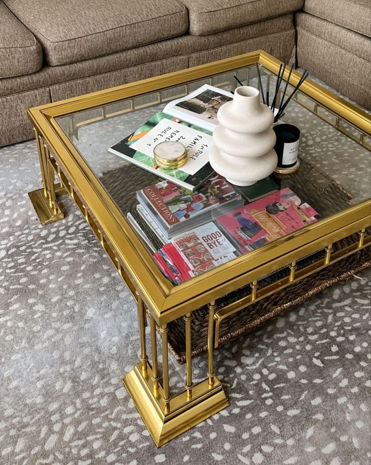 A brass and glass coffee table is filled with books and ornaments.