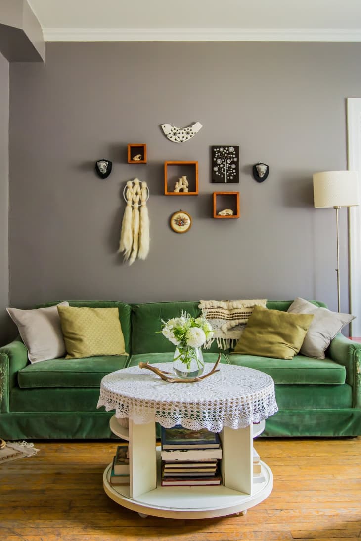a green velvet couch in front of a texture-rich gallery wall with shelves and textiles
