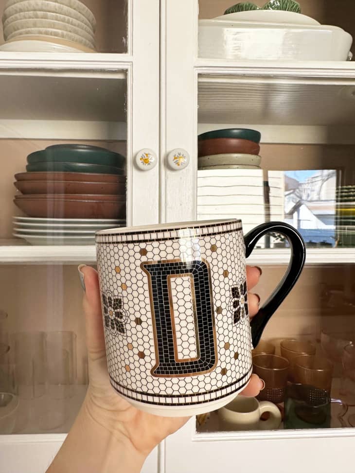 D tile mug held in front of glass front cabinets with dishes