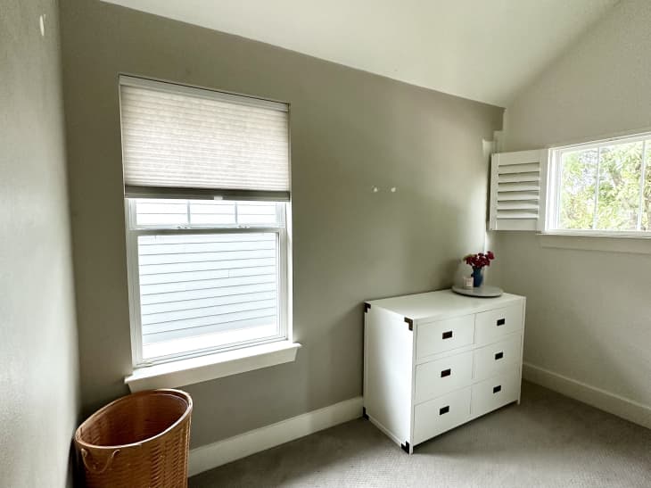beige walls with a white 6 drawer dresser, beige carpet and white shutters on small horizontal window