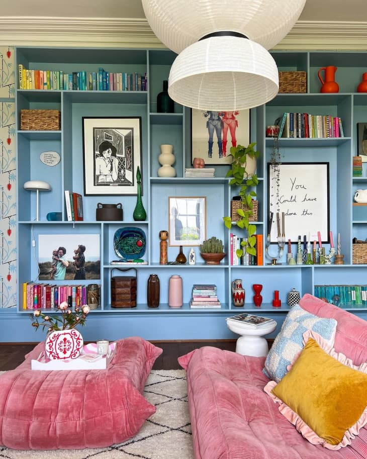 Room with floor to ceiling blue bookshelves with colorful books, artwork, candles, vases, and other types of decor