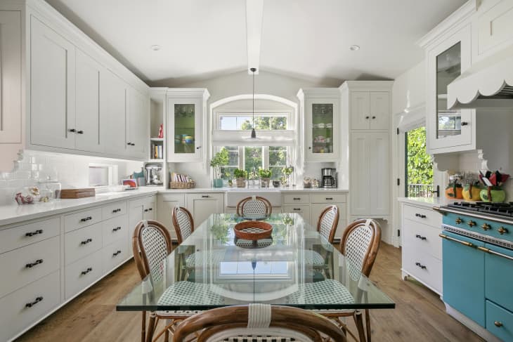 large white kitchen and dining area with turquoise oven and long glass top dining table