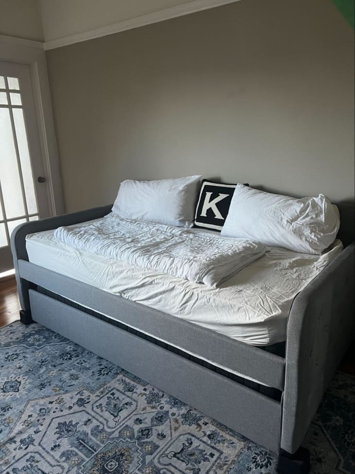 A grey trundle bed with white sheets