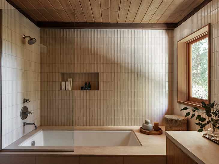Modern bathroom featuring a freestanding tub, tiled walls, wooden ceiling, and natural light from a window.