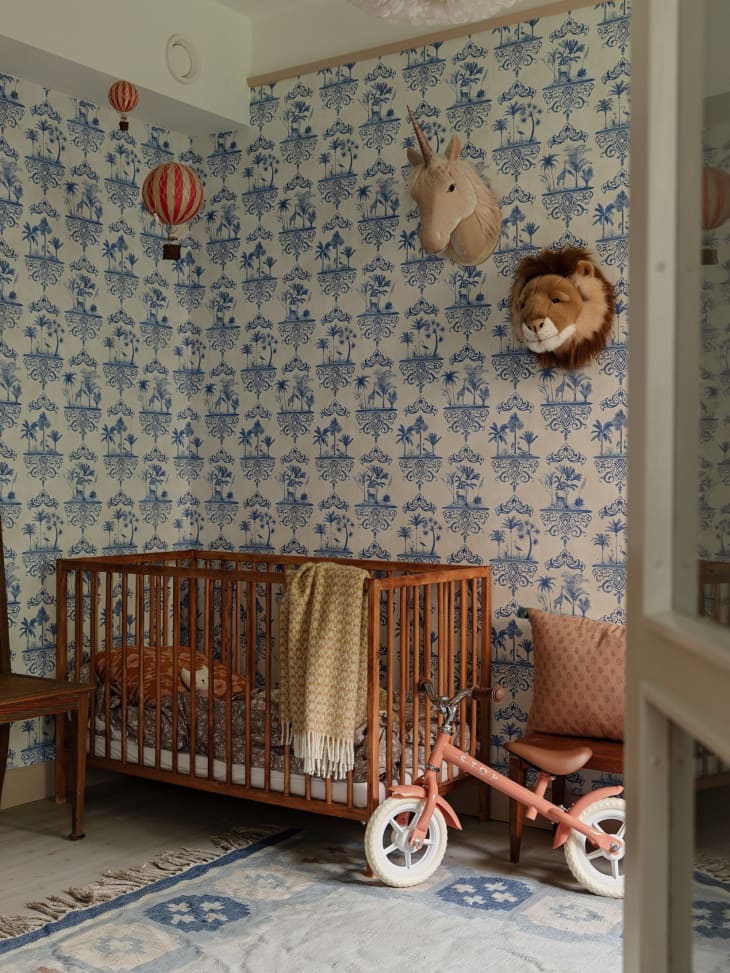 Blue vintage wallpaper behind crib with pink bike