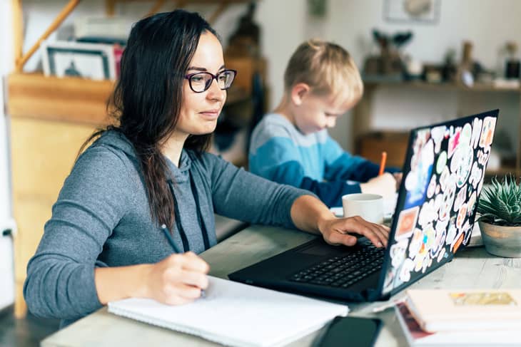 Mother on laptop while child creates next to her