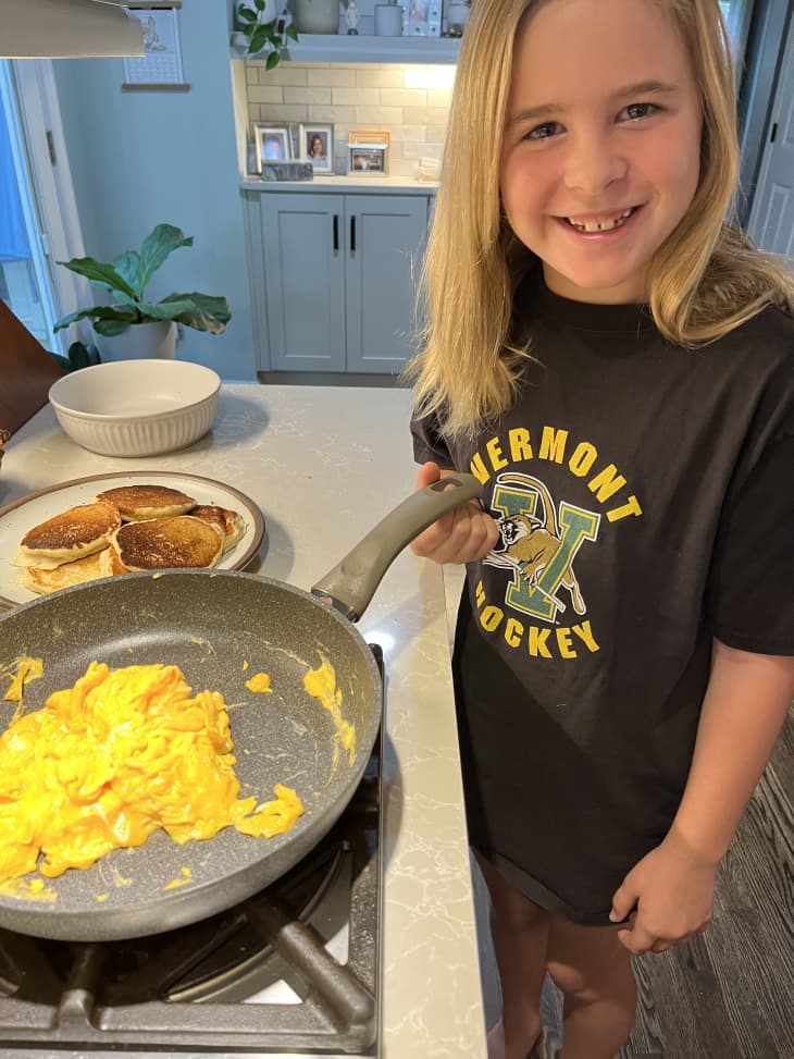 young girl smiling next to cooked eggs in skillet