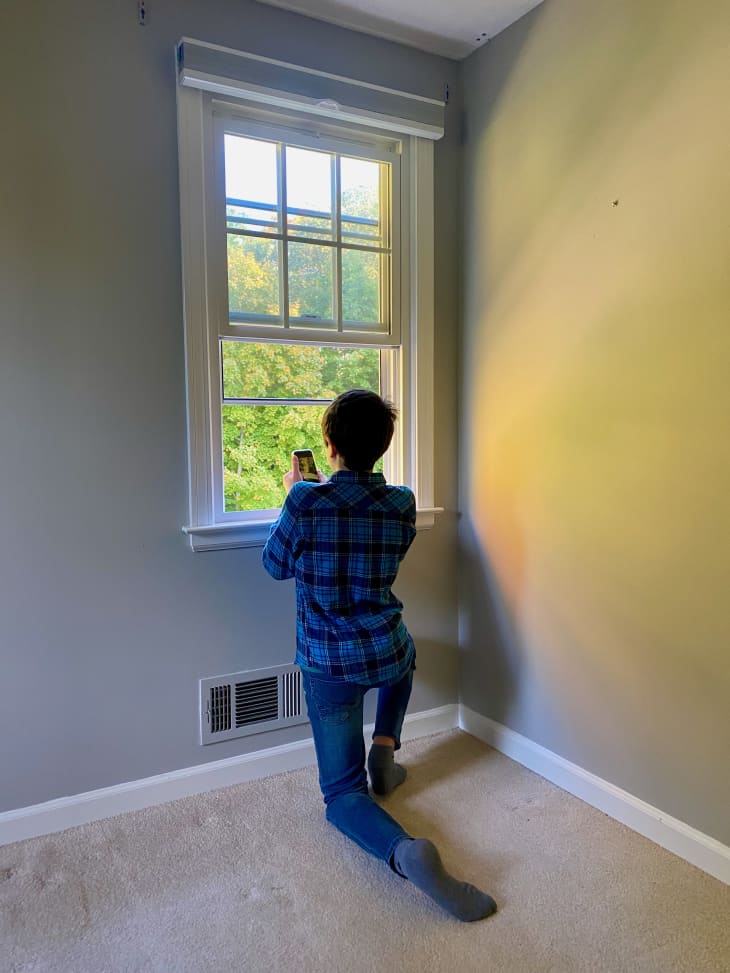 rear view of person kneeling on floor of empty room and taking photo out of the window