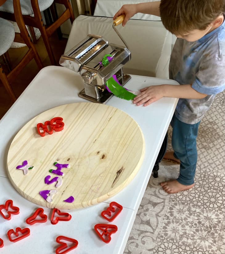 Kid using pasta maker to flatten play dough.