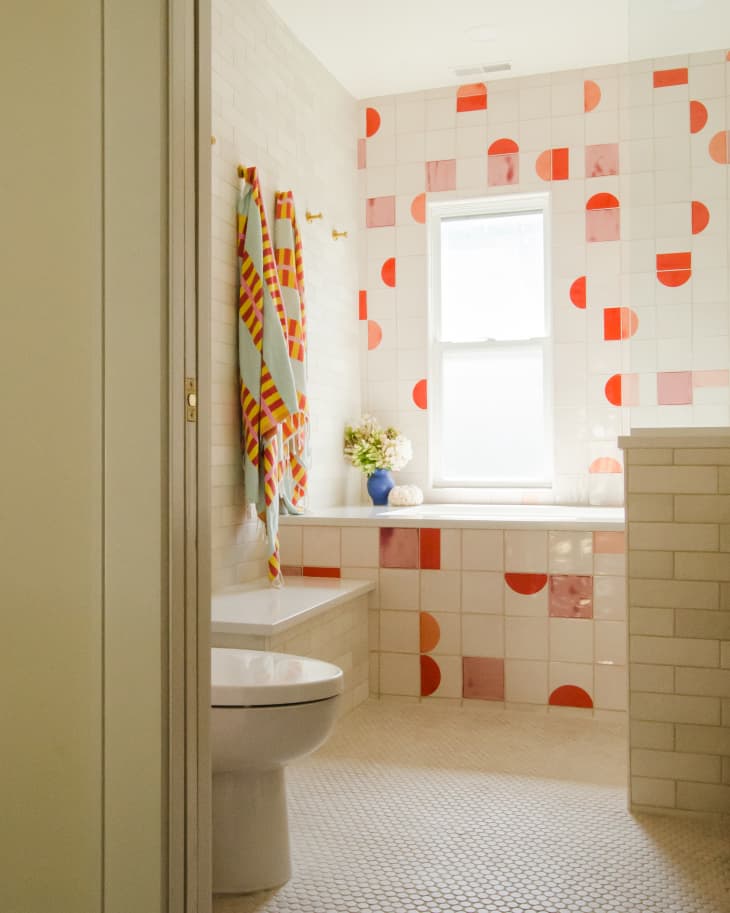 Kids bathroom with red, cream, and pink tile and large tub. White subway tile with aqua towels.