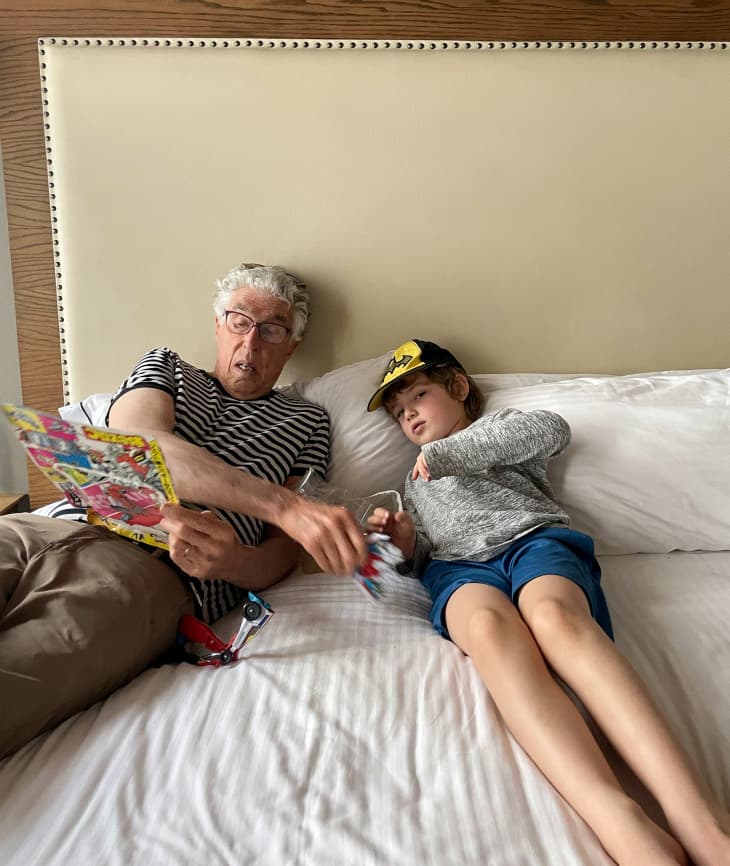 child and grandparent relaxing, reading on hotel bed