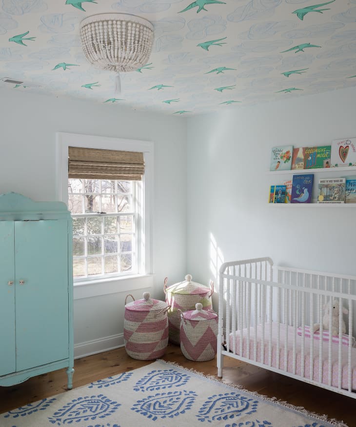 White nursery with aqua and blue bird wallpaper on ceiling, aqua wardrobe, and other pink and blue accents