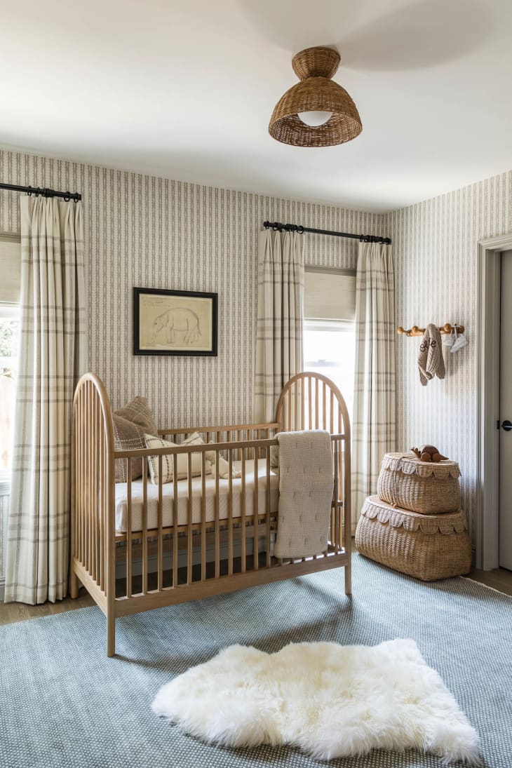 Nursery with taupe striped wallpaper and lots of neutral tones with blue rug