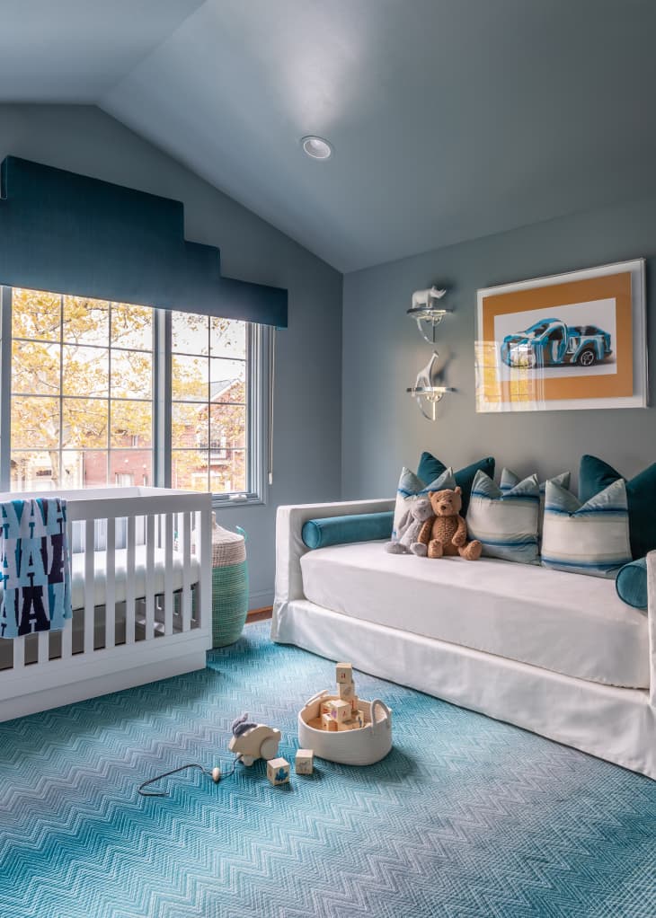 blue nursery with blue patterned rug, and white furniture with blue decor accents