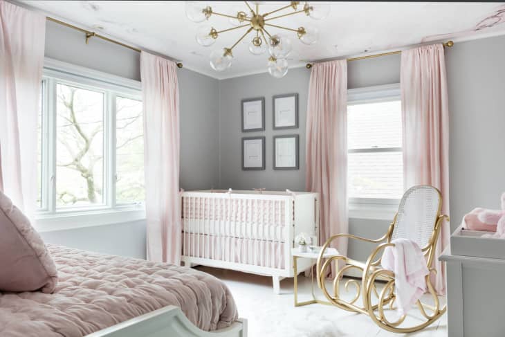 grey walls, white crib, rattan rocking chair, pink curtains, blush day bed, sputnik lighting fixture