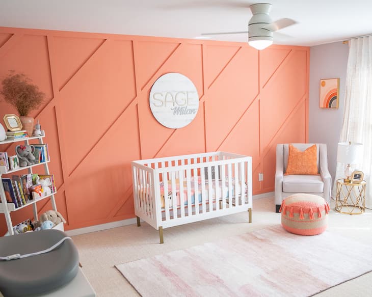 orange accent wall with wood trim, white crib, beige carpet, orange accent pillows