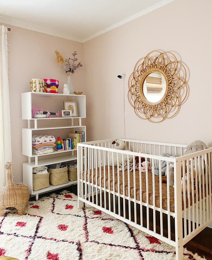 peach beige walls, cream rug with red and brown diamond accents, white crib, vintage gold floral shaped mirror