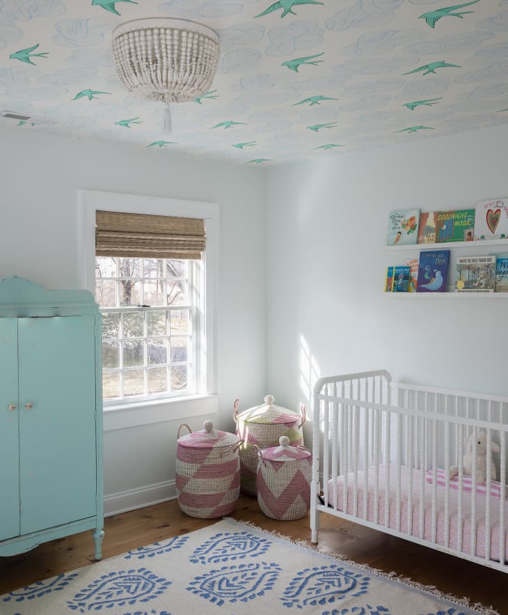 Light teal wardrobe, white crib, bird wallpaper on ceiling, bamboo roman shades
