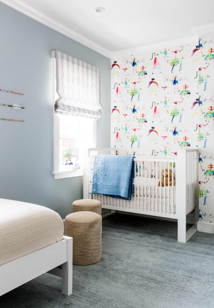 pale blue nursery with pale blue carpet, white crib, and people print wallpaper