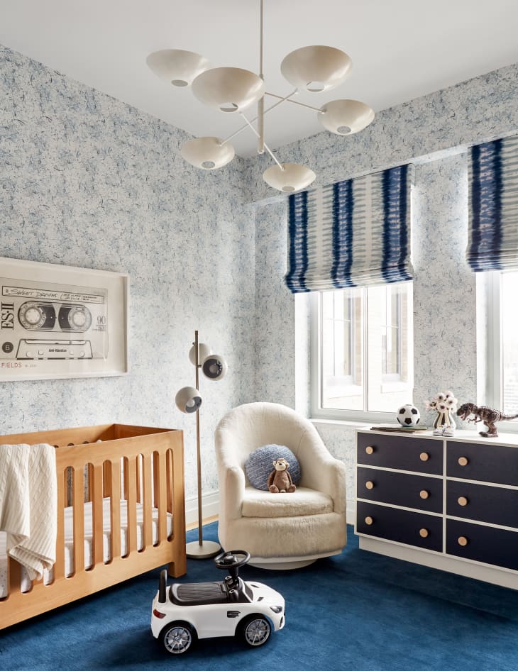Nursery with blue carpet, patterned blue and white wallpaper, and blue and white window shades