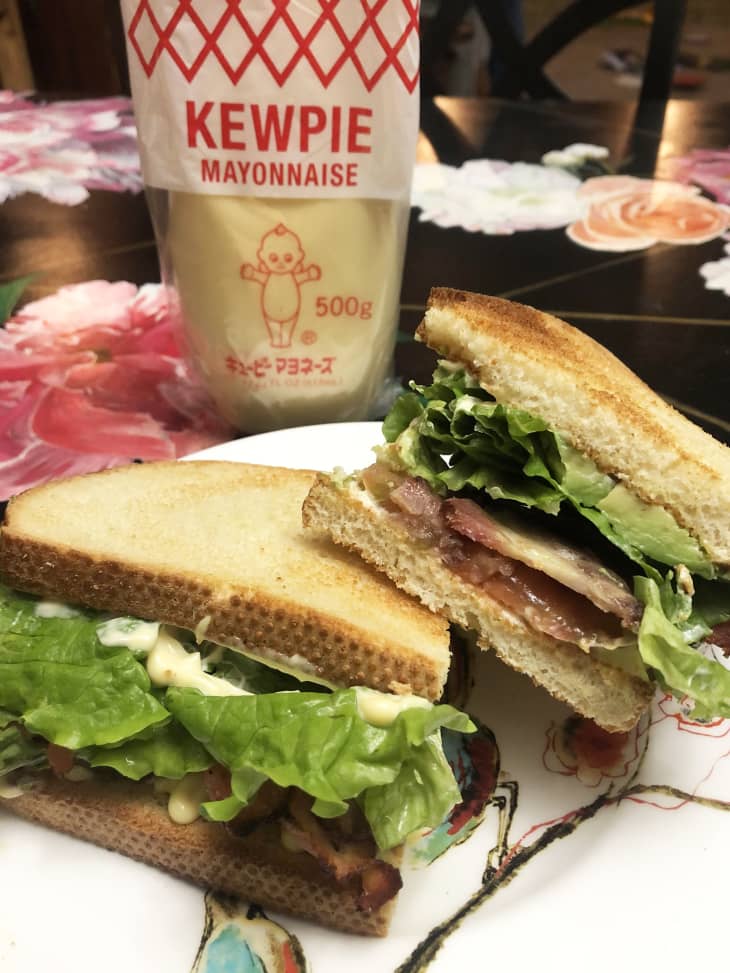 BLT sandwich on a colorful plate with a bird design, resting on a black table. In the background, a bottle of Kewpie mayonnaise standing up.