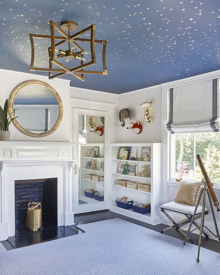 safari themed bedroom for kids, with starry ceiling wallpaper, large mirror above a fireplace, and a bookshelf in the lefthand corner. Telescope.