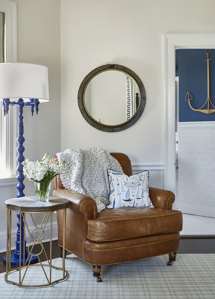 nautical themed bedroom with leather chair in center of frame. mirror above leather chair, along with metal end table and blue and white floor lamp.