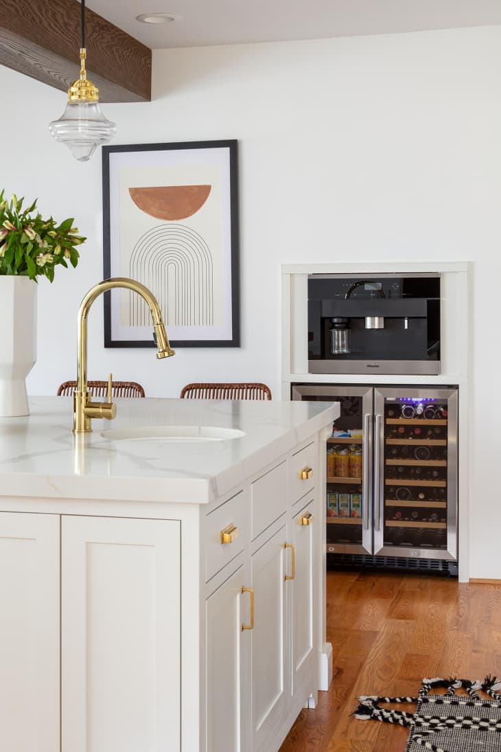 Light and airy kitchen with brass faucet and sink in kitchen island. Modern art on walls. A drink fridge built under an espresso bar.