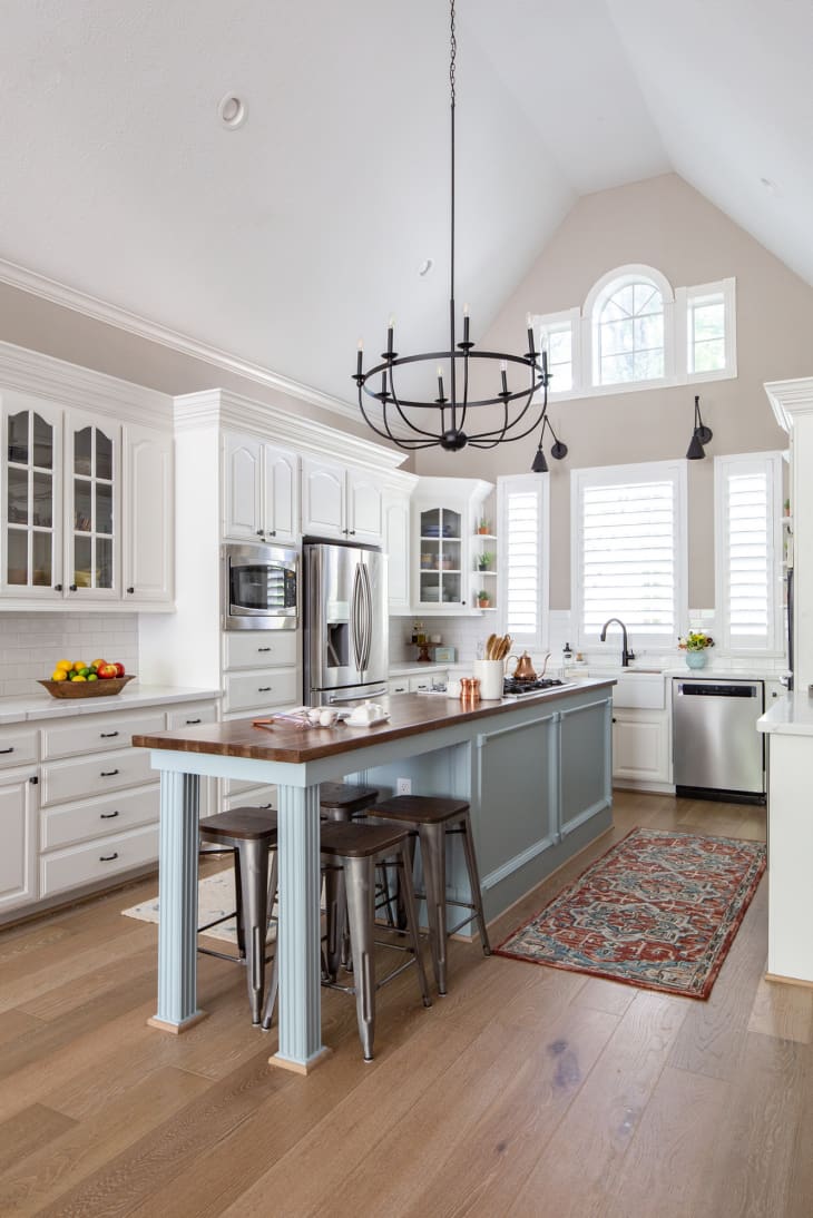Open kitchen with vaulted ceilings and an iron, stark chandelier. Lots of open windows and light, white cabinets, and a kitchen island that extends to a table for four.