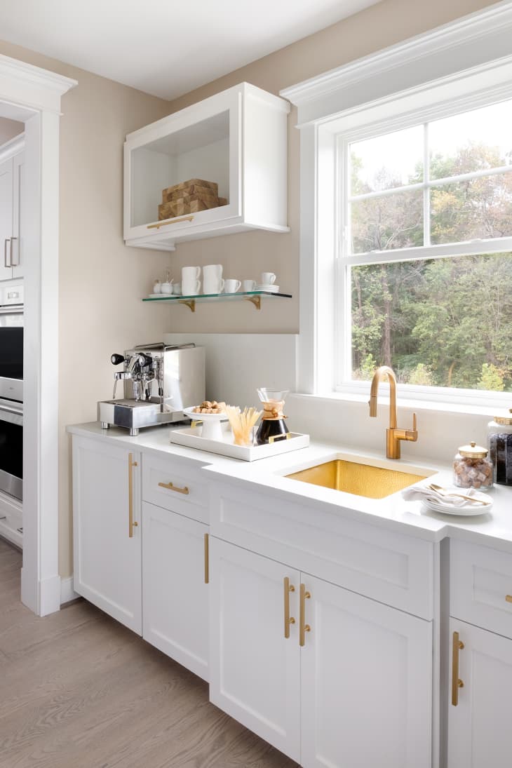 Kitchen facing white cabinets and sink. Open window onto clean space, with gold sink and faucet.