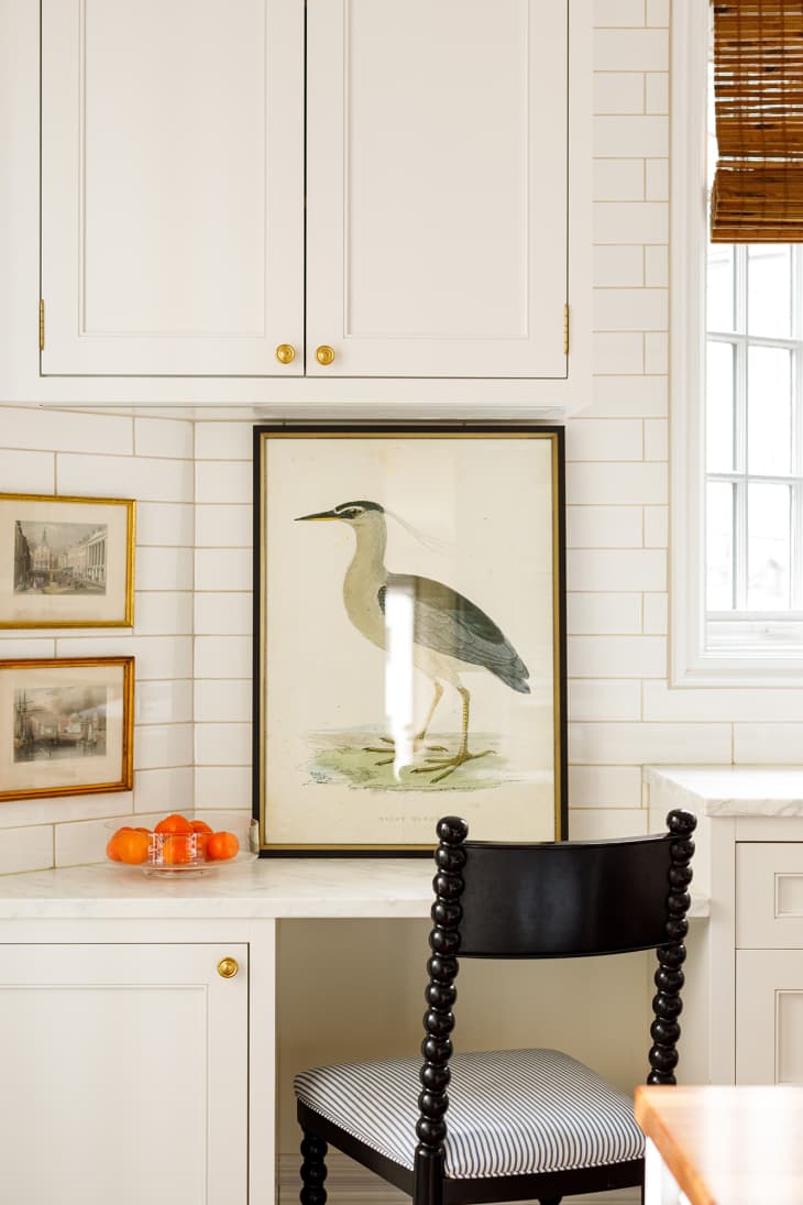 Homework nook in a kitchen with tiled backsplash, and vintage natural art, including a bird in a black frame.