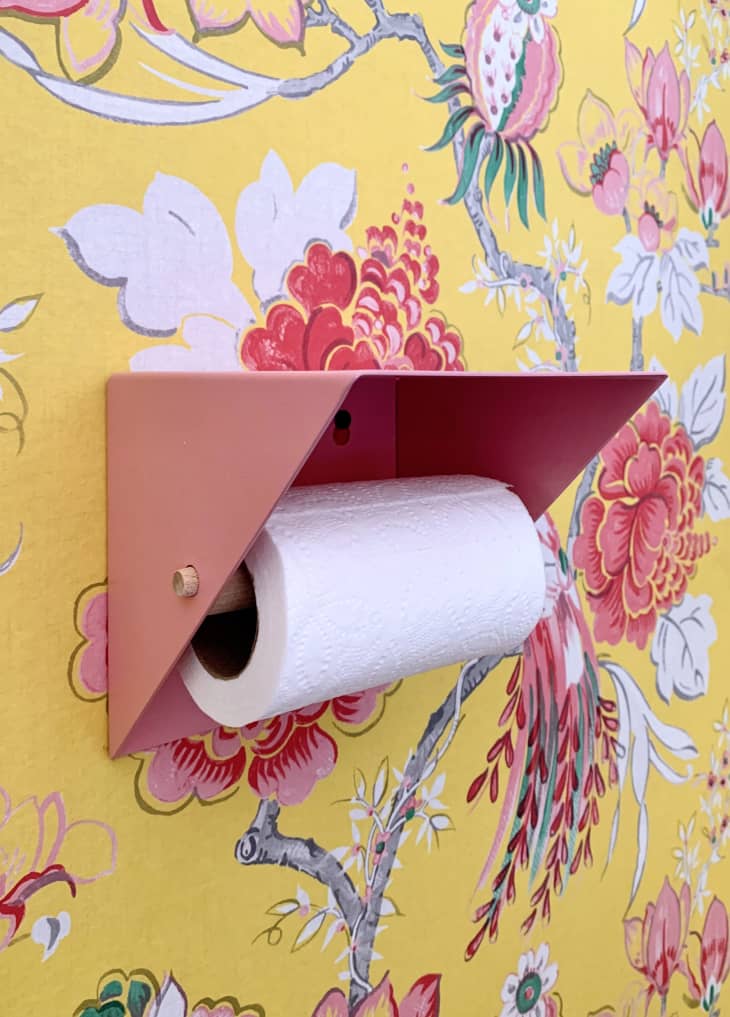Close-up of canary yellow printed wallpaper, and a slim pink toilet-paper holder.