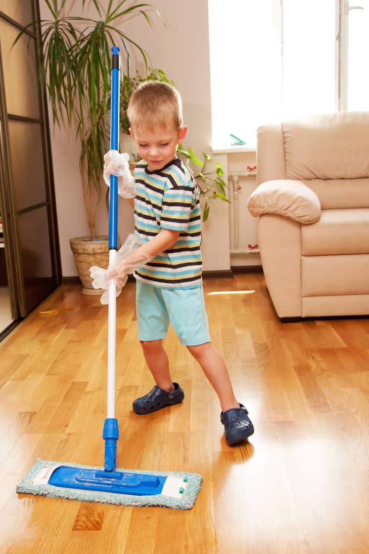LIttle boy dusting on floor in front of a clean room.
