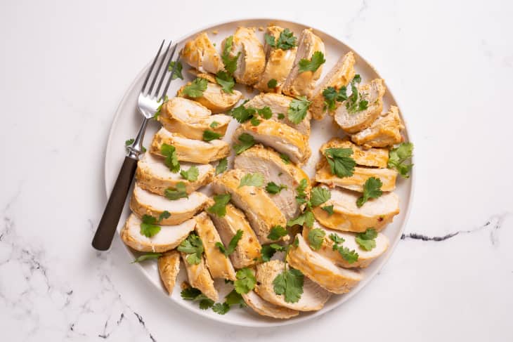 Cooked sliced chicken arranged neatly on a white platter with a fork