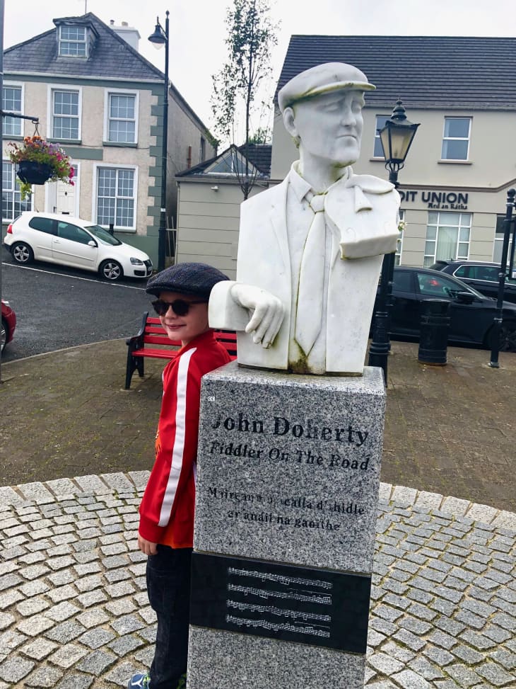kid in red coat in front of John Doherty statue in Ireland