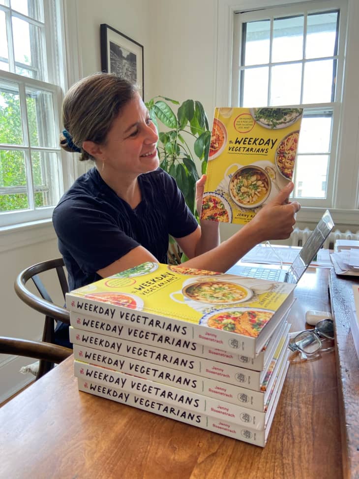 Jenny Rosenstrach holding up her new cookbook, Weeknight Vegetarian. stack of same cookbooks next to her
