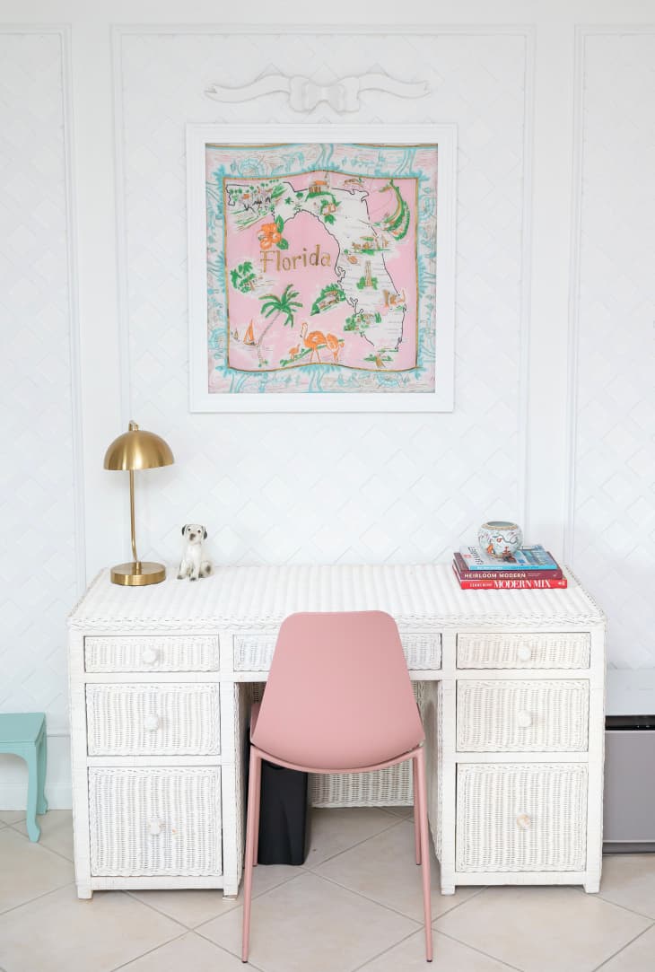 white room with white desk. Pink chair at desk and gold desk lamp with white dog detail. Pink and blue print of Florida on wall above
