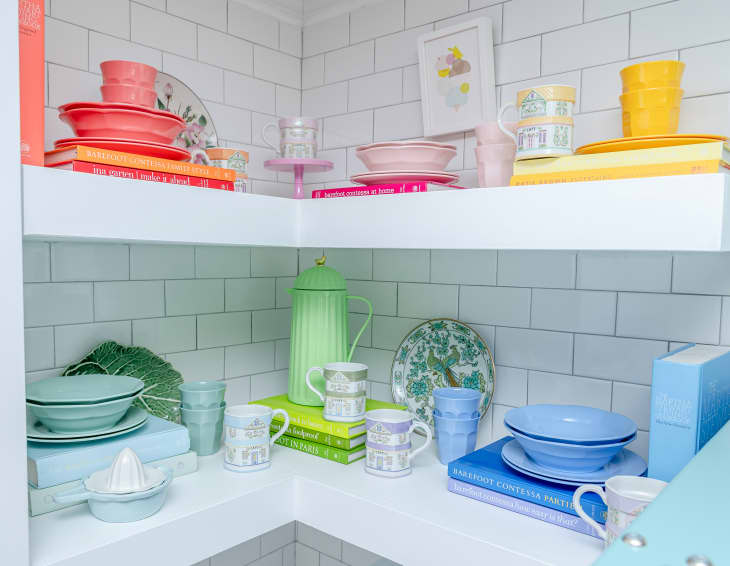 white shelves in a kitchen with colorful dishes and white tile walls behind