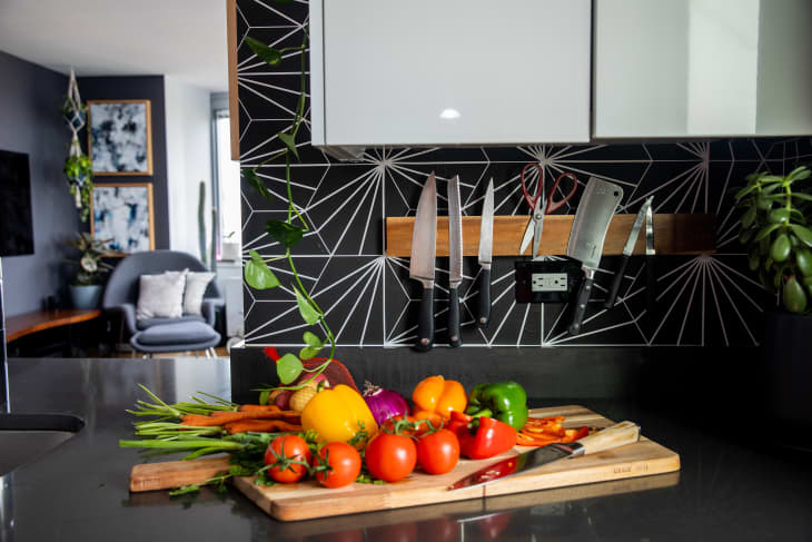 Kitchen scene with vegetables on cutting board, knife rack in back, living room in distance