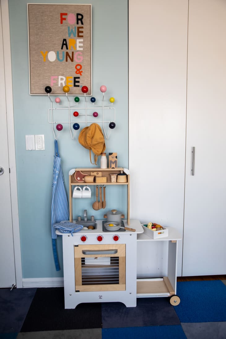 Kids' kitchen set with stove, oven, shelf, dishes. Colorful wall hooks above and a bulletin board with colorful letters on it