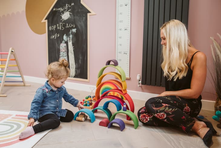 mom plays with daughter and a colorful stacking rainbow toy in playroom